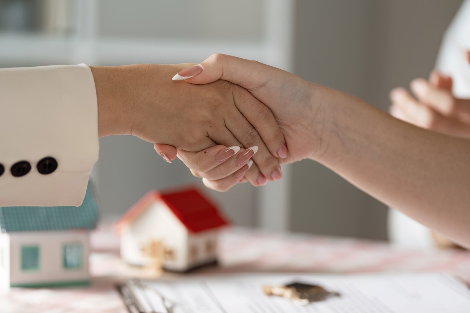 Real Estate Agent Shaking Hands with Client Over Contract and Model House on Table